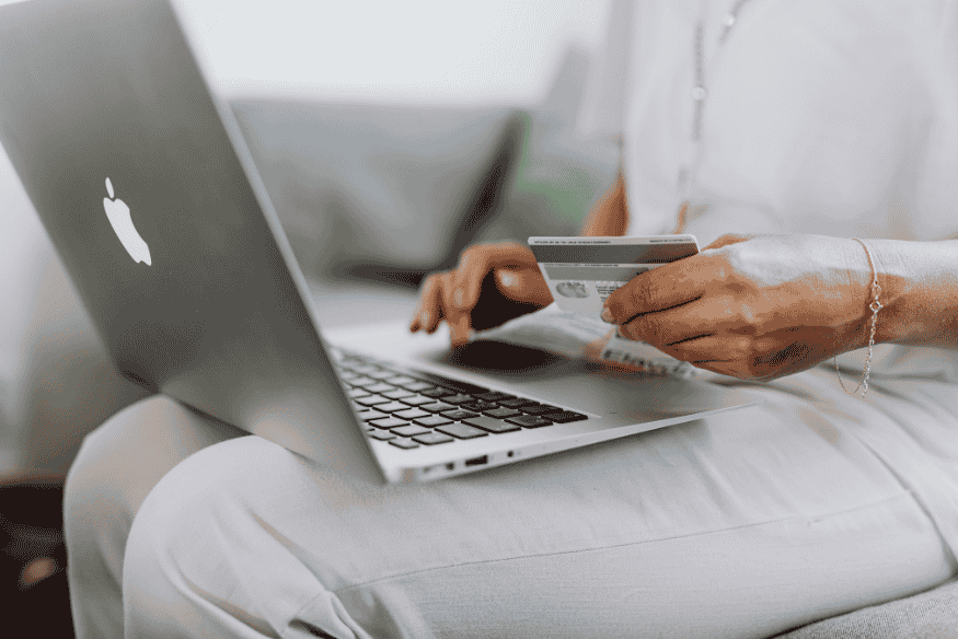 Person holding a credit card while shopping online on a laptop at home.