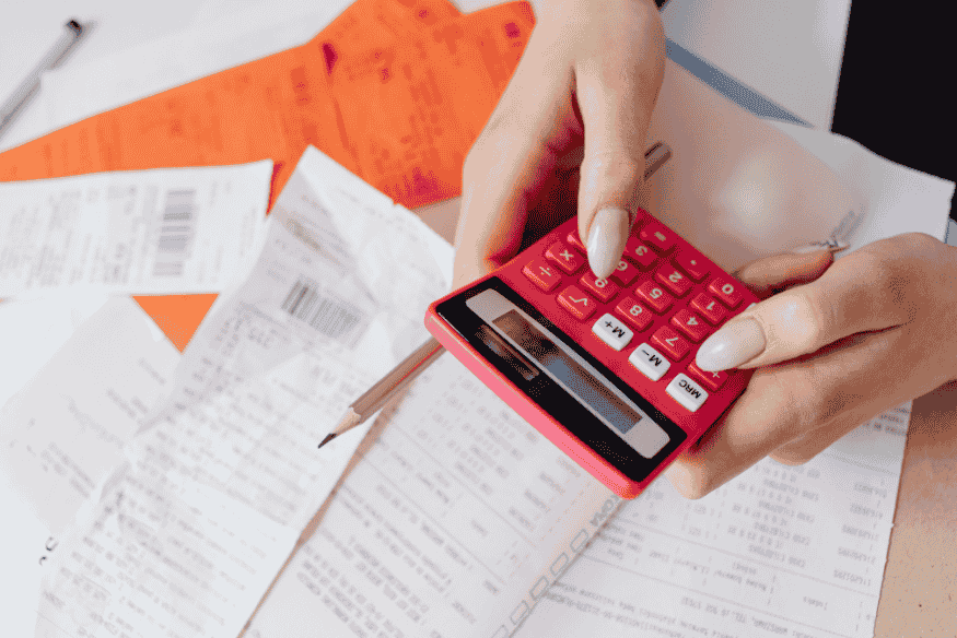 Person using a calculator over bills and receipts to compare costs, fees, and repayment plans between Buy Now Pay Later and credit cards