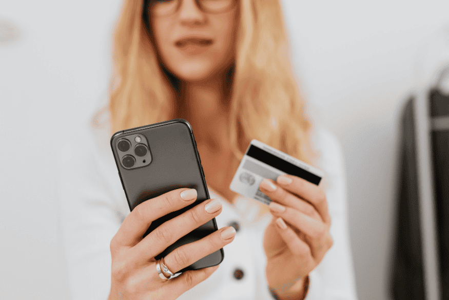 Woman holding a smartphone and credit card while managing finances online.