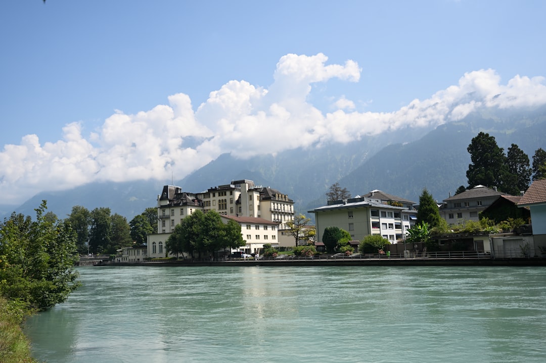 Buildings line a wide river with mountains behind.