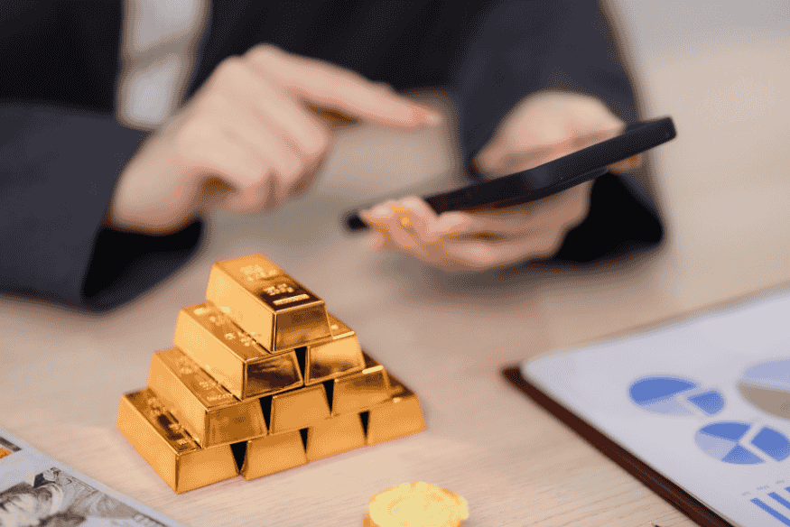 Person using a smartphone near stacked gold bars symbolizing digital tools for wealth management.