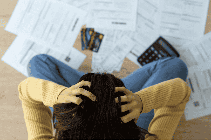 Woman sitting on the floor stressed while surrounded by bills, credit cards and a calculator.