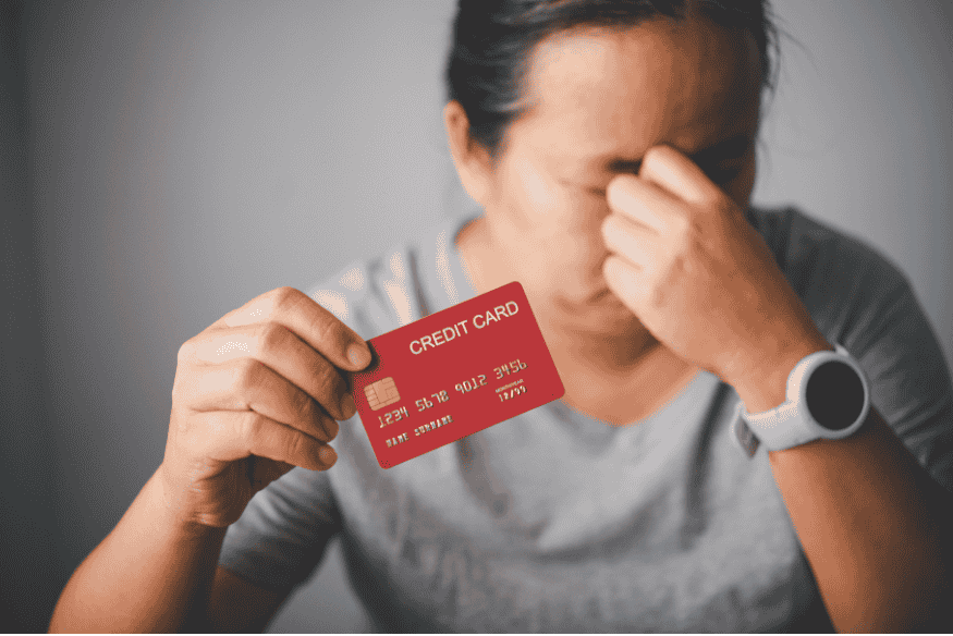 Worried woman holding a red credit card and rubbing her forehead in financial stress.