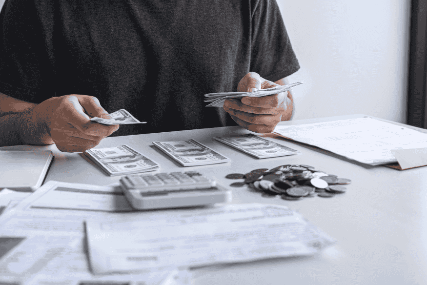 Person counting dollar bills at a desk with calculator, coins, and bills while organizing a simple monthly budget plan
