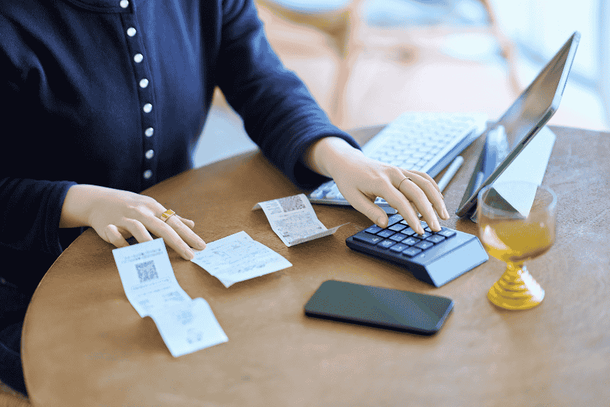 Person reviewing receipts with a calculator and tablet to track daily personal expenses