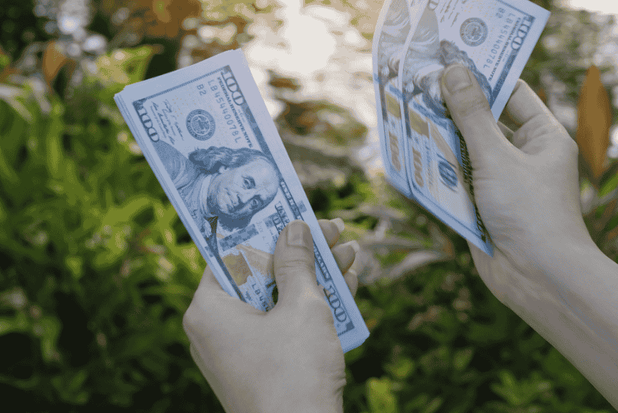 Person counting stacks of hundred-dollar bills outdoors, representing personal cash inflow.