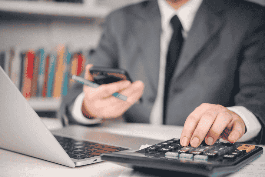 Financial manager using laptop, phone and calculator to project future revenue with simple models