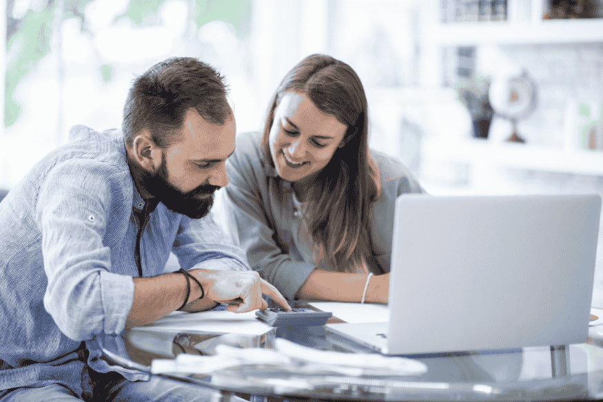 Couple sitting at a table with a laptop and calculator, planning their household budget and organizing personal finances together.