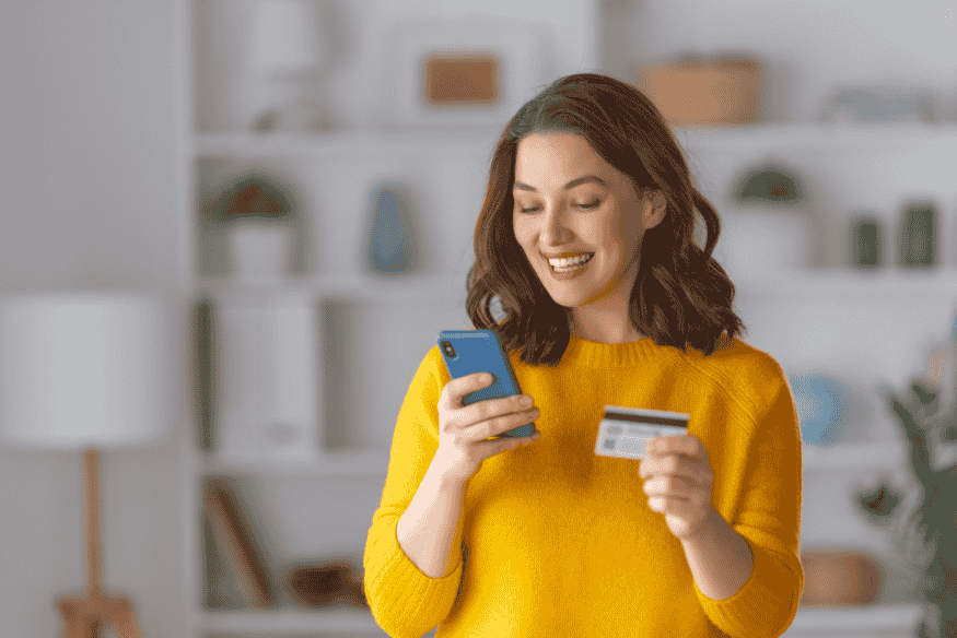 Woman holding a credit card and using her phone while planning a big purchase without going into debt.
