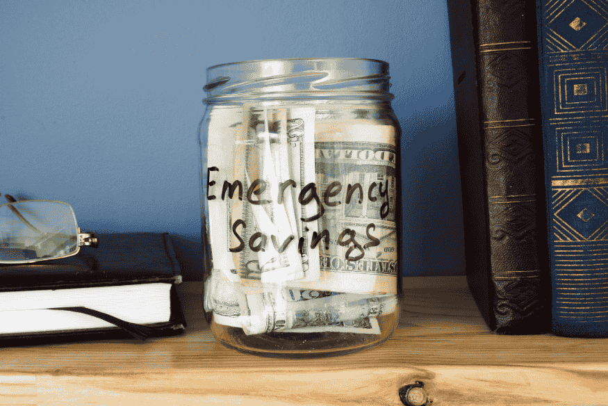 Glass jar labeled emergency savings filled with cash for business emergency planning