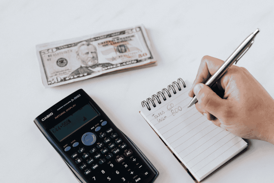 Close-up of a person using a calculator and notepad with cash on the table to plan taxes and loan payments, showing basic expense tracking and budgeting.