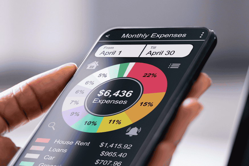 Hand holding a smartphone displaying a colorful monthly expenses pie chart, representing digital expense tracking apps that simplify money management.