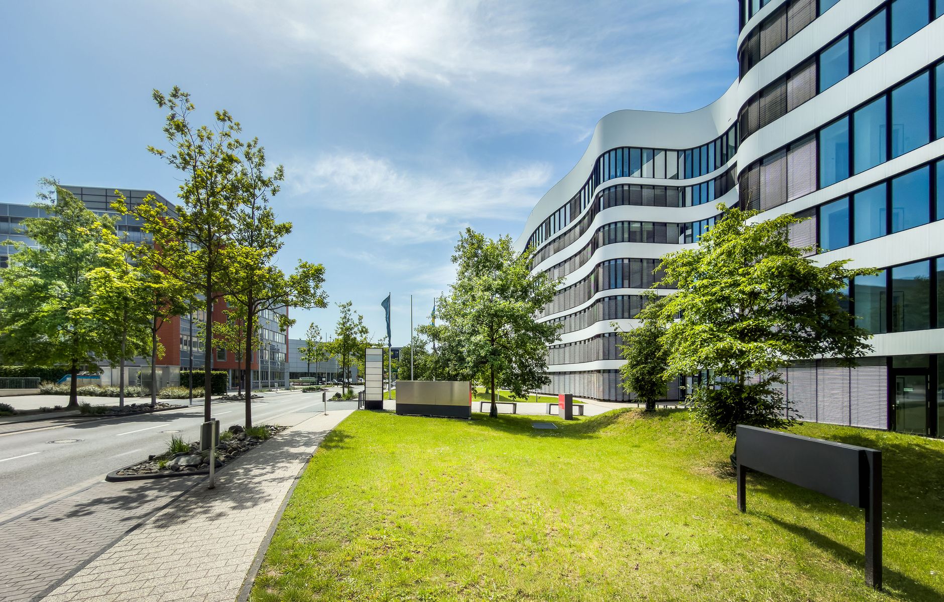 Contemporary business office building with curved architecture and trees in an urban setting.