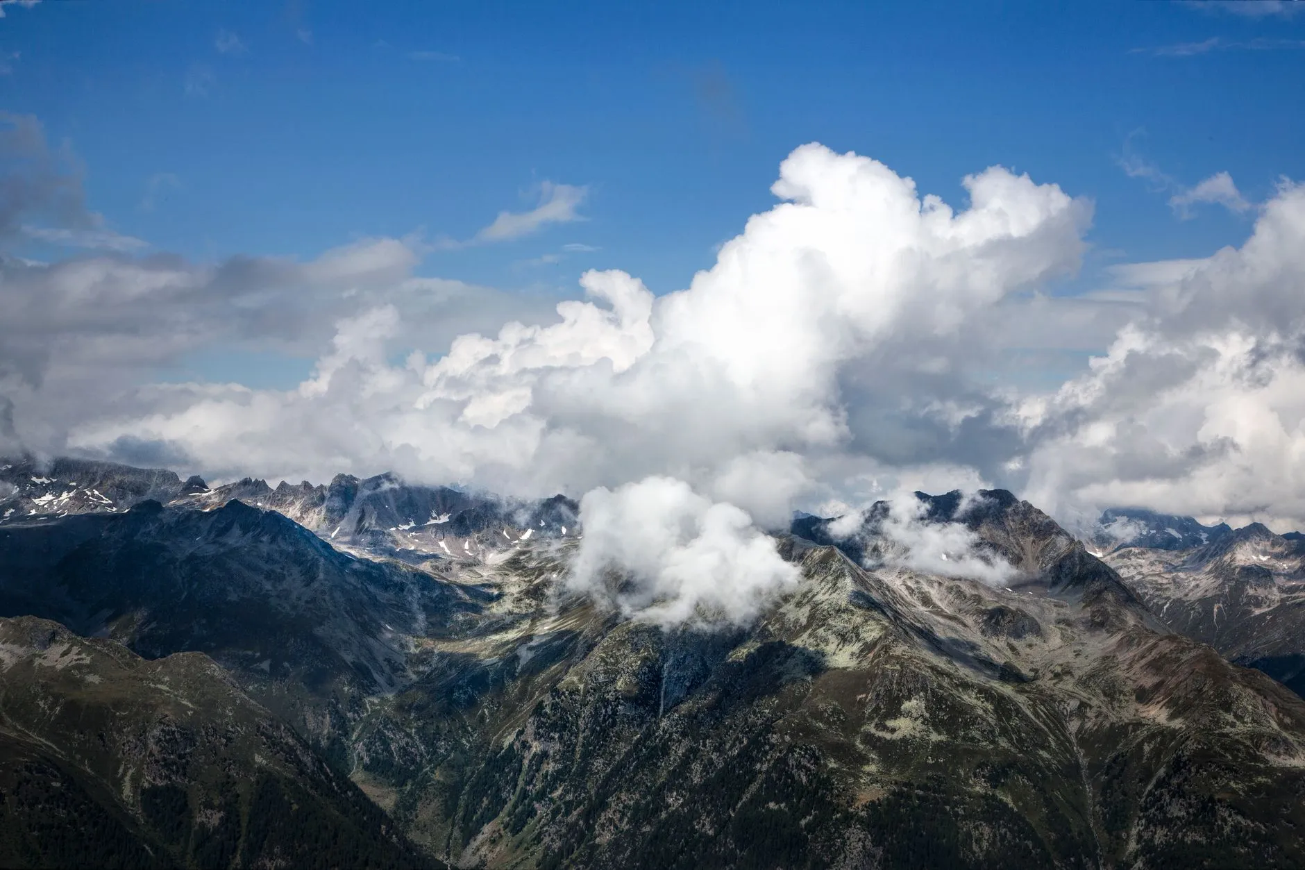 A breathtaking aerial view of a rugged mountain range with clouds over the peaks.
