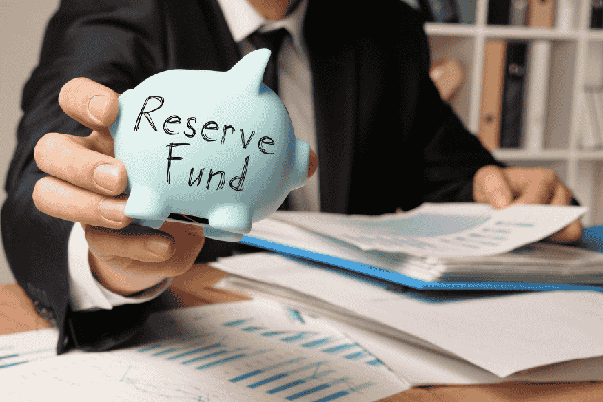 Businessperson holding a piggy bank labeled reserve fund to illustrate sinking funds for planned expenses